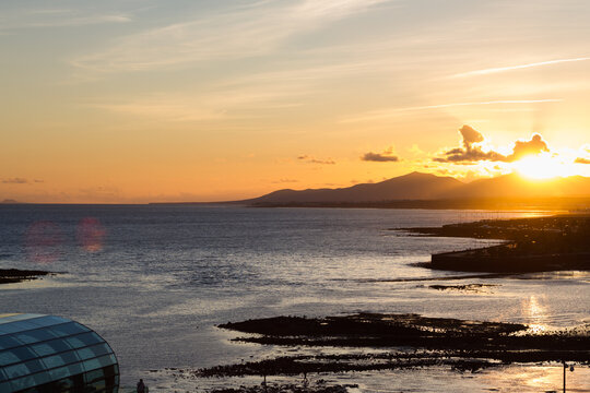 Backlight of mountains over the sea at sunrise. The golden sun sets behind the silhouettes of the mountains. Golden clouds over the ocean. Lanzarote, Canary Islands, Spain.