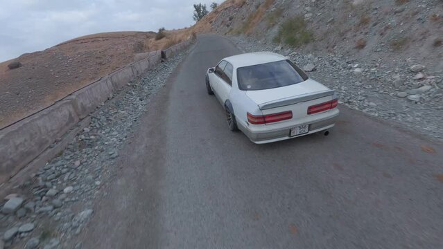 Korch jdm speed drift racing extreme driving on mountain serpentine asphalt road turning around aerial view. FPV sports drone shot white car drifting burning smoke diffusion race spin track cliff 4k