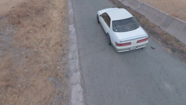 Around speed drift racing extreme driving on mountain serpentine asphalt road turning around aerial view. FPV sports drone shot white car drifting burning smoke diffusion race spin track cliff 4k