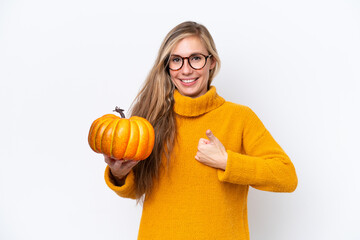 Young blonde woman holding a pumpkin isolated on white background with thumbs up because something...