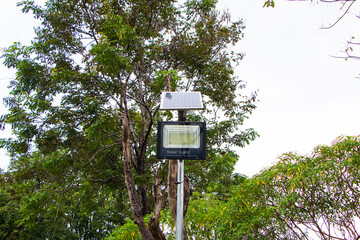 Solar panel powered street light bulbs side walking street in park.  saving electricity by using solar energy as renewable energy. Sky cloud was overcast and tree green is background.