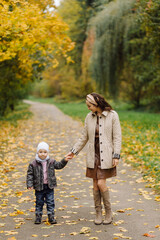 Fototapeta premium Mom and son walking and having fun together in the autumn park.