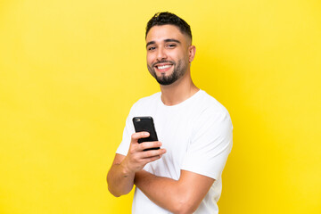 Young Arab handsome man isolated on yellow background holding a mobile phone and with arms crossed