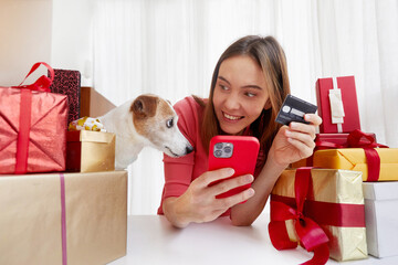 Happy female with smartphone and credit card smiling and looking at cute Jack Russel Terrier dog...