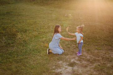 Naklejka na ściany i meble Young mother and daughter, hugging and playing in a golden field of sunshine