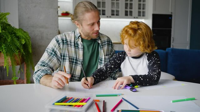 Redhead boy helps father draw picture and man smiles