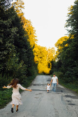 Fototapeta premium Happy family in a park in summer autumn. Mother, father and baby play in nature in the rays of sunset