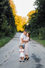 Happy family in a park in summer autumn. Mother, father and baby play in nature in the rays of sunset