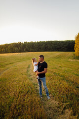 Naklejka na ściany i meble Happy family in a field in autumn. Mother, father and baby play in nature in the rays of sunset.