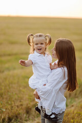 Fototapeta premium Happy family in a field in autumn. Mother, father and baby play in nature in the rays of sunset