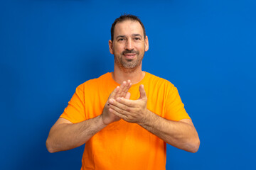 Hispanic handsome elegant man over blue isolated background.Clauping and clapping happy and joyful, smiling proud hands together