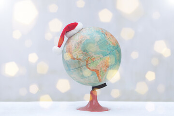 globe with christmas hat on snow. bokeh flare Santa Claus Hat as travel concept