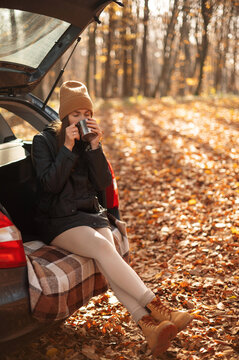 Vertical view of the caucasian girl sitting in open car trunk and enjoying of hot tea