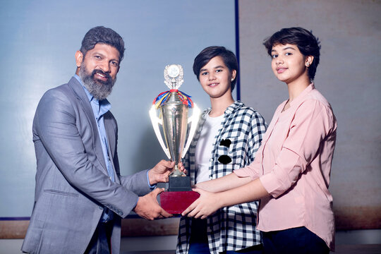 Indian man school teacher give victory trophy cup to girl students, Female receive winning prize.