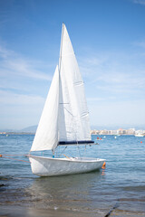 Obraz premium small white sailboat with white sails moored near the beach
