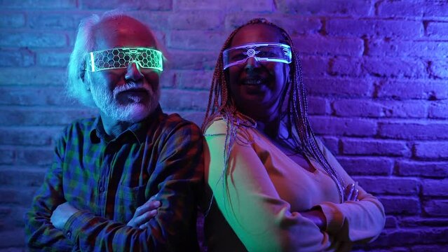 Happy elderly friends having fun with futuristic augmented reality glasses, multiracial couple Asian male and Hispanic American female - Metaverse Concept
