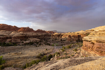Water Canyon, located in the Maze District of Canyonlands National Park in Utah seen at sunset on a spring day. A few small, unidentifiable hikers are seen in the dry wash..
