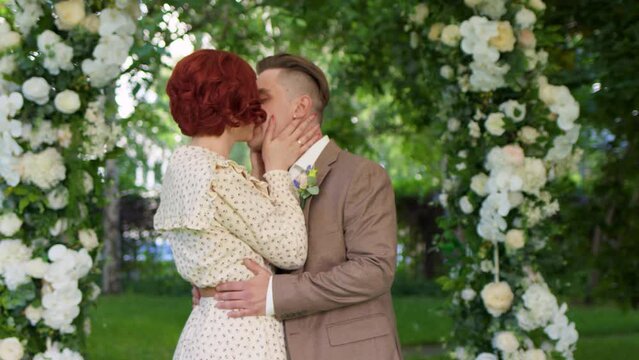 Young and beautiful bride and groom stand against backdrop of flower arch in park and are about to get married. wedding ceremony of two heterosexual people at exit registration of marriage.