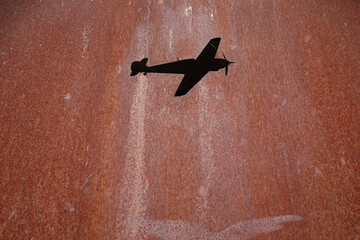 A hole in the shape of an airplane in rusting metal
