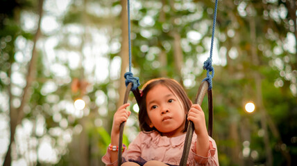 Portrait dreamy funny little girl riding on swing in the twilight with nature background