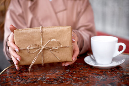 woman drinking coffee or cappuccino in french cafe on street. hands hold gift box sitting at table in pastry shop or bakery
