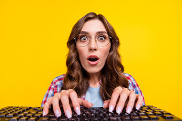 Portrait of excited speechless woman curly hairstyle checkered shirt typing keyboard impressed looking isolated on yellow color background