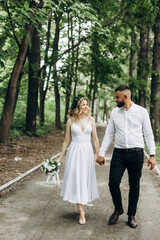 Fototapeta premium A happy young couple in love walk in a garden. A man in a white shirt and a girl in a white light dress are walking in a park