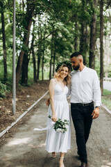 Fototapeta premium A happy young couple in love walk in a garden. A man in a white shirt and a girl in a white light dress are walking in a park