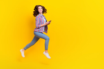 Fototapeta na wymiar Full length photo of positive girl with wavy hairdo checkered shirt hold phone fast online delivery isolated on yellow color background