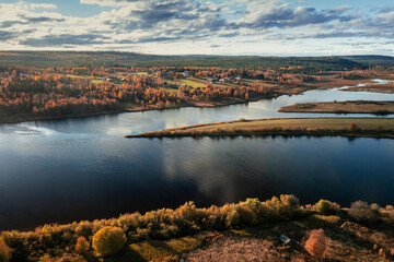 River with trees in autumn shades and a small village with wooden cottages on its banks