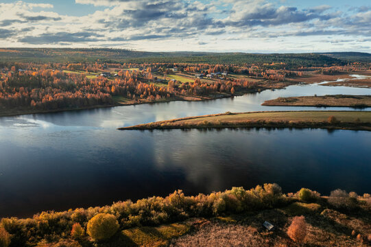River with trees in autumn shades and a small village with wooden cottages on its banks