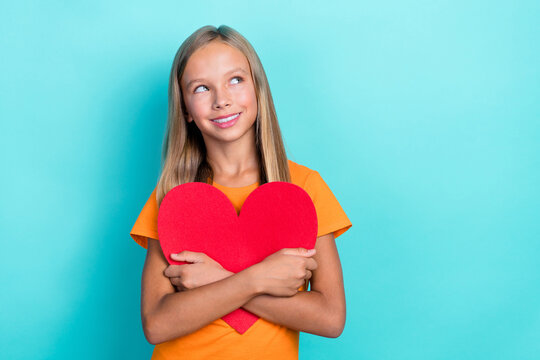 Photo of little dreamy schoolgirl kid hug her big red paper heart positive looking interested youtube blog channel empty space isolated on cyan color background