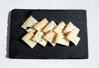 Aged goat cheese slices on a black stone plate, white surafce background, isolated close-up, Tenerife, Canary Islands, Spain