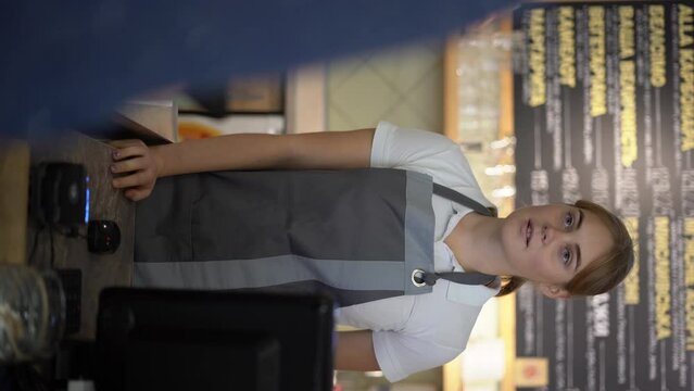 Smiling waitress barista saleswoman on coffee shop counter, woman client pay in cafe with phone via pos machine using nfc terminal make contactless mobile payment.