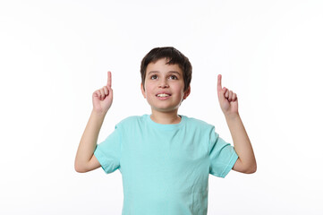Portrait on white background Caucasian smart school boy, teenager, wearing blue turquoise t-shirt, smiling a beautiful toothy smile, pointing fingers up at advertising space for your promotional text.