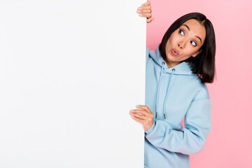 Photo of adorable impressed lady wear blue hoodie holding looking blank billboard empty space isolated pink color background
