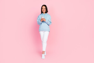 Full length photo of dreamy sweet lady wear blue hoodie communicating modern device walking...
