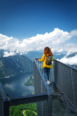 Redhead girl in yellow jacket is looking at  Hallstatter lake, Hallstatt and surrounding mountains from 5 Fingers view point in Austria. Dachstein mountains.