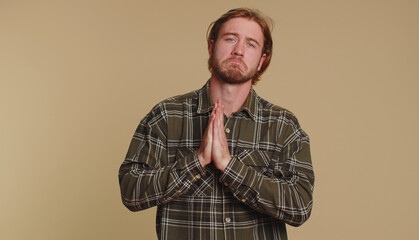 Obraz premium Please, God help. Sad worried man praying, looking upward, making wish asking with hopeful imploring expression begging apology, forgiveness. Young adult guy indoor isolated alone on beige background