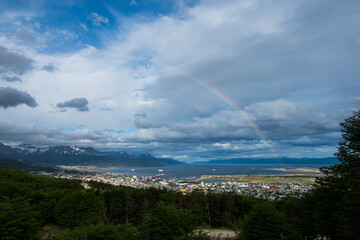 View of the Mountains surrounding the city of Ushuaia that flows into the harbor.  With a rainbow over the city.