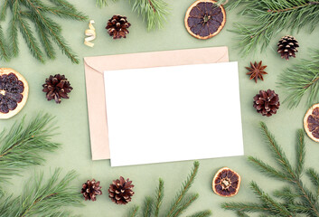 Winter holiday layout made of spruce, pine branches, natural xmas decor and white blank on green background. Top view Flat lay Mock up. Xmas or New Year template