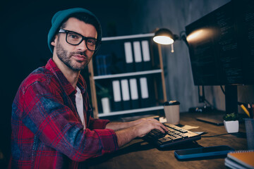 Photo of cool serious coder dressed hat glasses fulfilling task modern gadget indoors workplace...