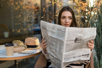 An attractive girl reads a newspaper in the park. Surveillance private detective monitors the...