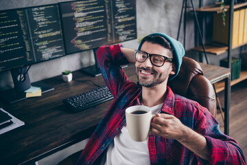 Photo of dreamy good mood freelancer wear hat glasses hand behind head enjoying coffee indoors workplace workstation loft