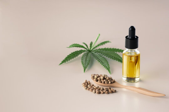 Legalized marijuana concept features with CBD oil extract from marihuana in glass bottle with dropper lid, piles of hemp seeds on empty background. Marijuana products for copyspace and advertising.
