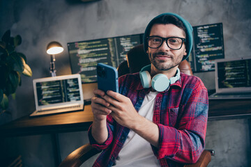 Photo of smiling positive coder dressed hat glasses headphones creating ebank ecard app modern...