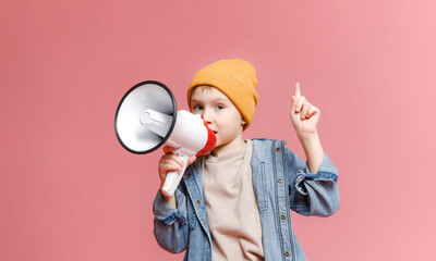 cute 7-8-year-old schoolboy in jeans and a hat, holding in his hand and speaking into an electronic...