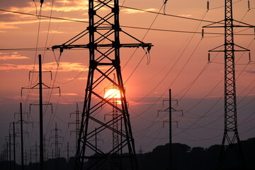sun inside the silhouettes of power pylons, sunset and evening time on a summer evening