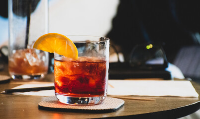 Colorful red cocktail on ice with a slice of orange adoring the glass rim. 