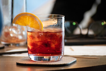 Colorful red cocktail on ice with a slice of orange adoring the glass rim. 